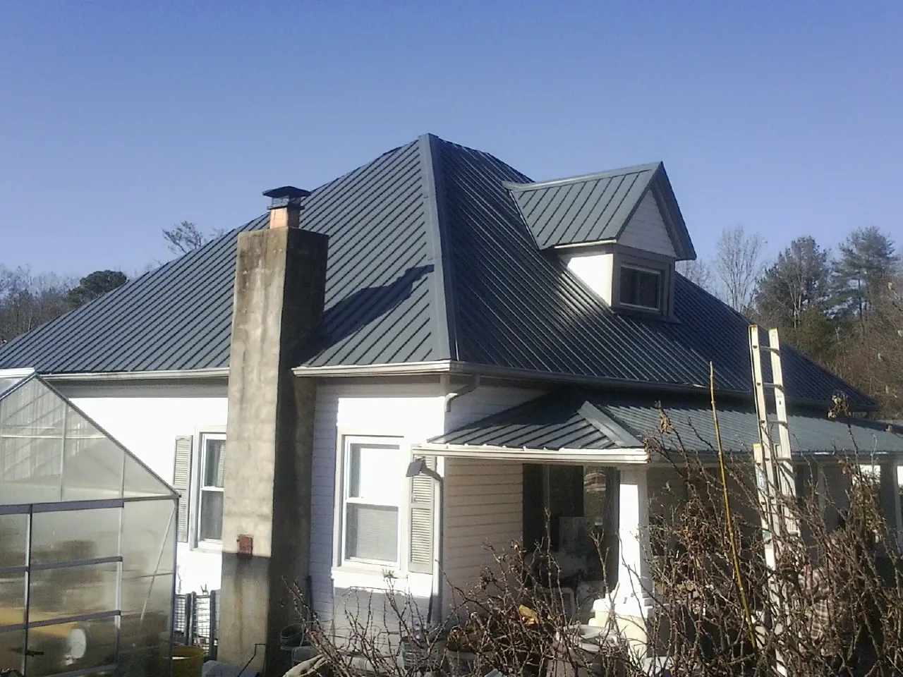 Dark blue standing seam metal roof on a white farmhouse with dormer — Slate & Tile Roof Repair by Roofing Brothers in Western Springs