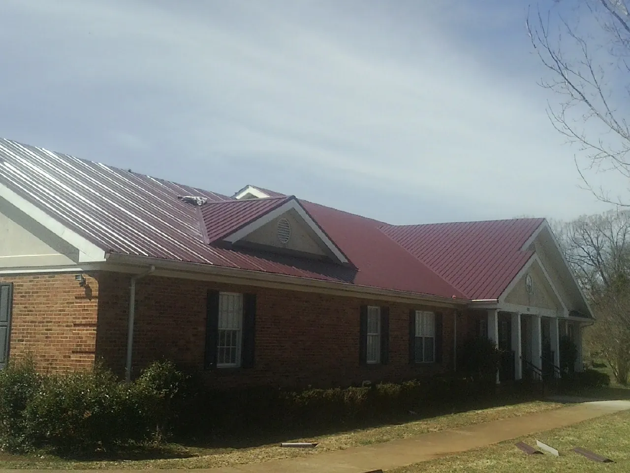 Red metal roof with gabled entries on a long brick building, from a Hail Damage Roof Repair job in Western Springs