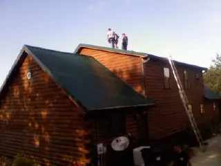 Crew on the ridge of a green metal roof on a two story log home in Western Springs