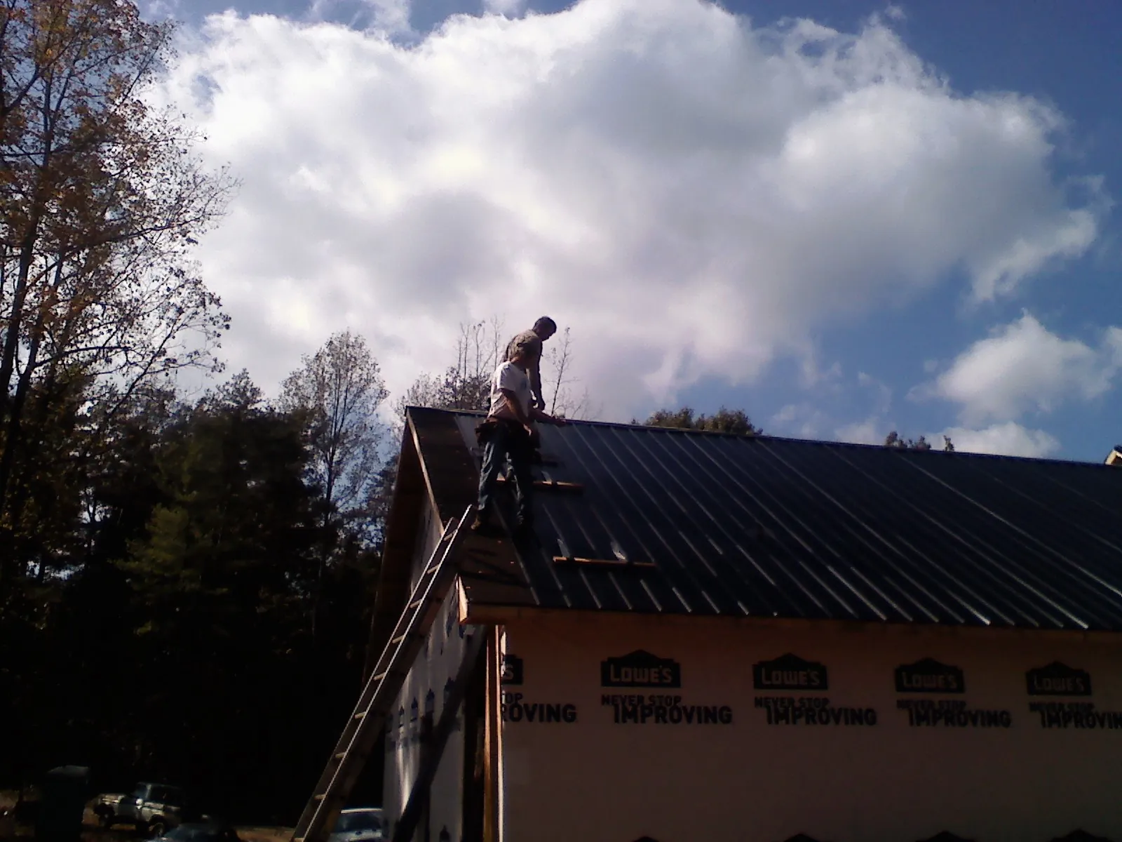 Roofer fastening dark metal panels high against a cloudy sky, from a Roof Inspection job in Western Springs