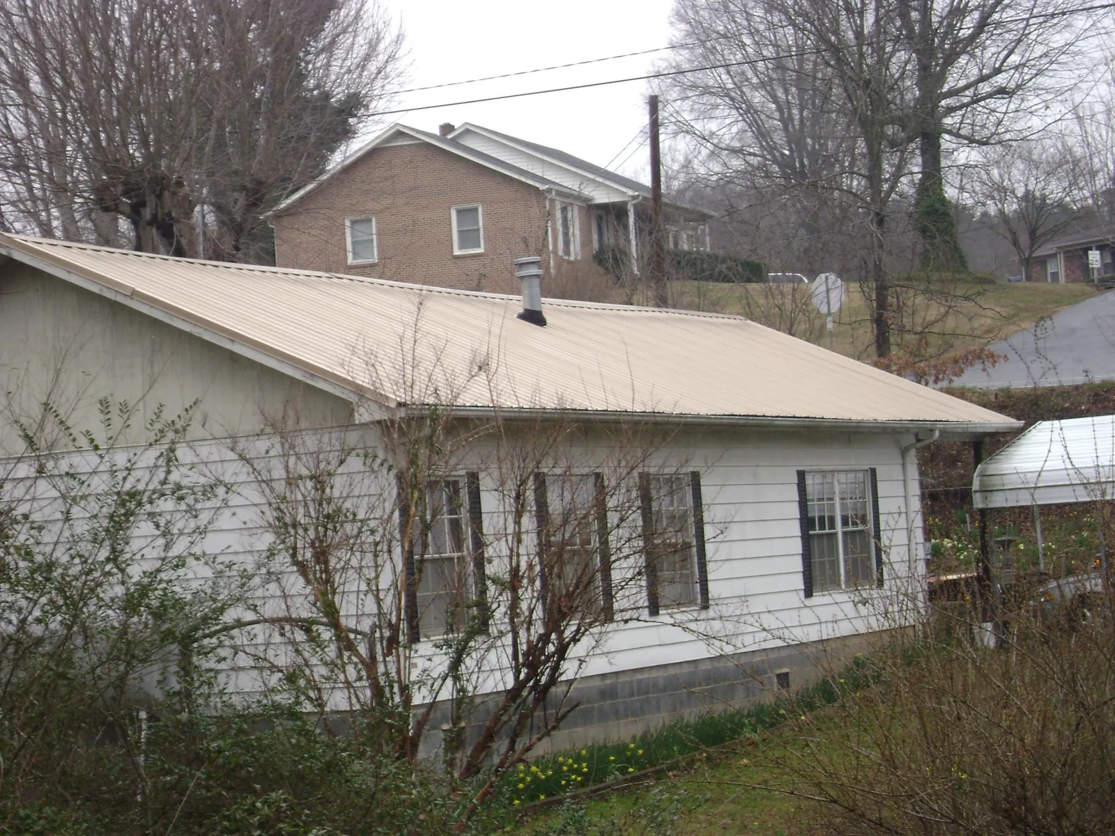 Tan metal roof on a white sided house set into a hillside — Commercial Roofing by Roofing Brothers in Western Springs